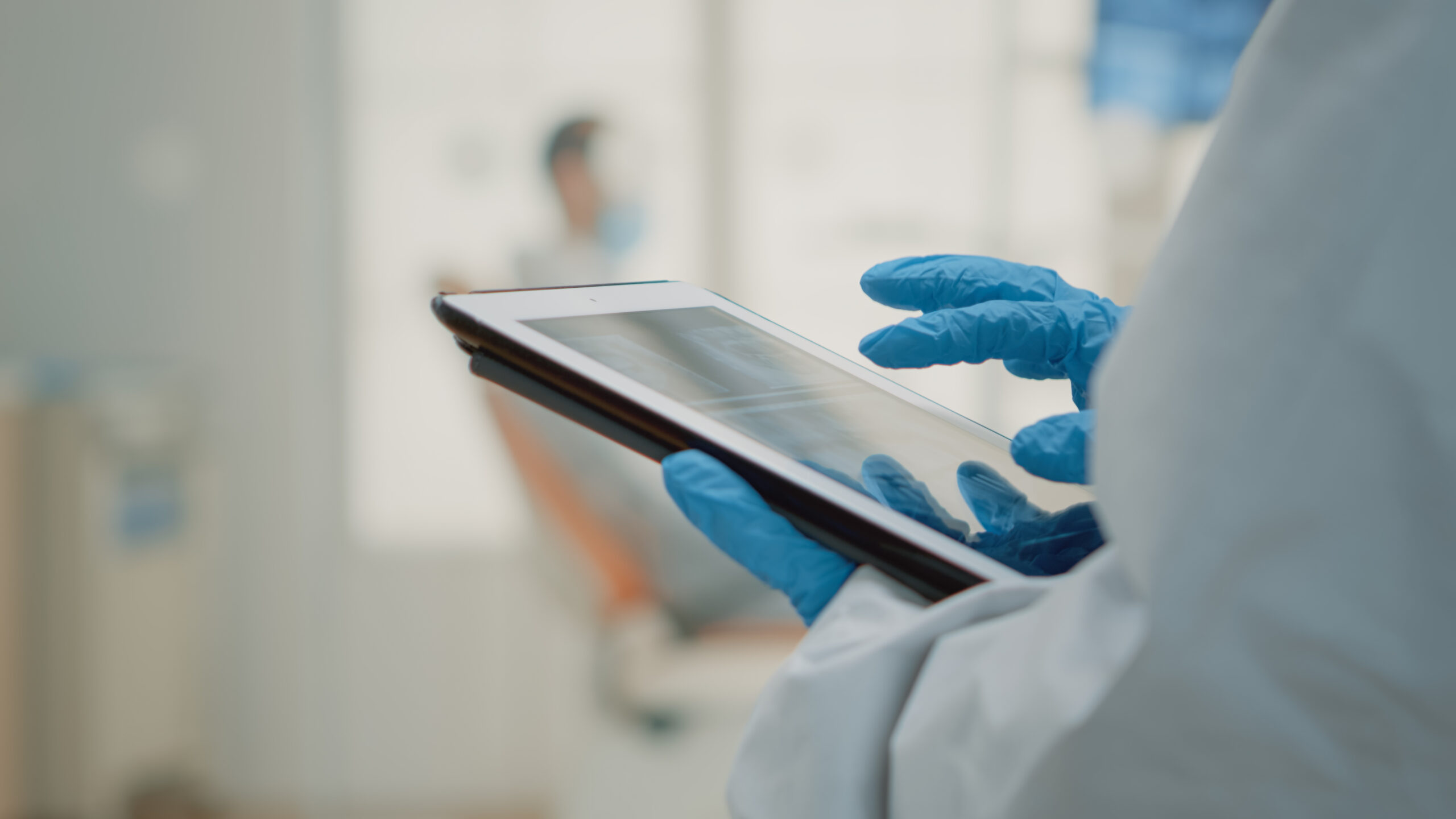 Dental professional wearing blue gloves reviewing digital patient information on a tablet