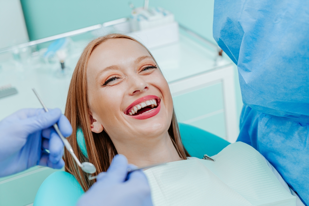 Laughing patient during a dental exam Woman laughing in a dental chair as gloved hands hold a mirror and instrument near her mouth