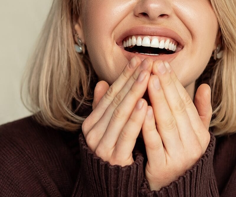 Close-up of a woman smiling with her hands held near her cheeks