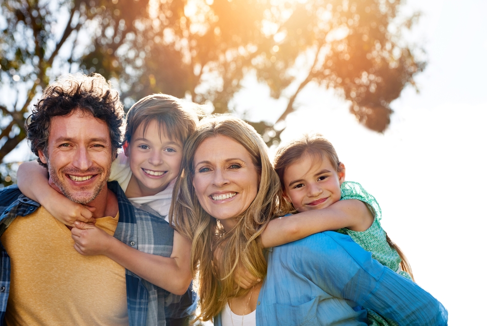 Smiling family portrait outdoors Family of four smiling outdoors with two children on their parents' backs