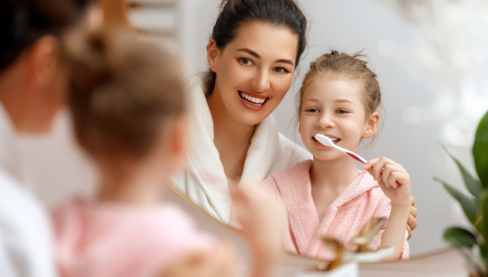 Mother helps her daughter practice brushing her teeth for healthy dental habits in San Marcos, CA