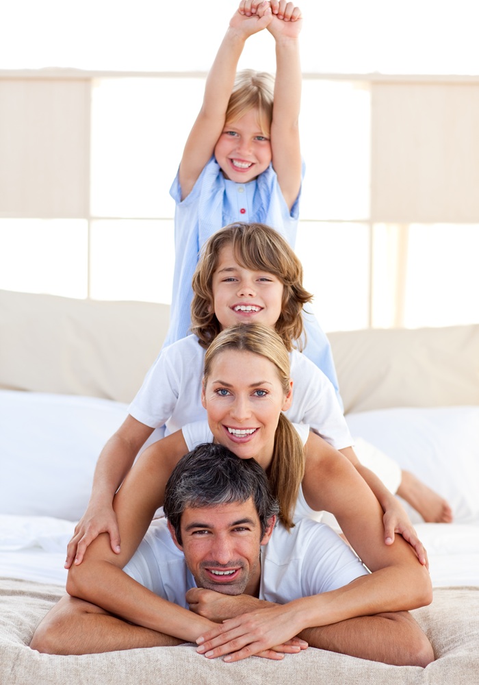 Smiling family portrait indoors Family of four smiling in a stacked pose on a bed, with the youngest child raising her arms
