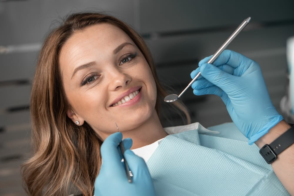 Patient in dental chair looking at camera and smiling. Beautiful and pretty woman. Hands with instruments at a dentist diagnosing a patient in a medical clinic.