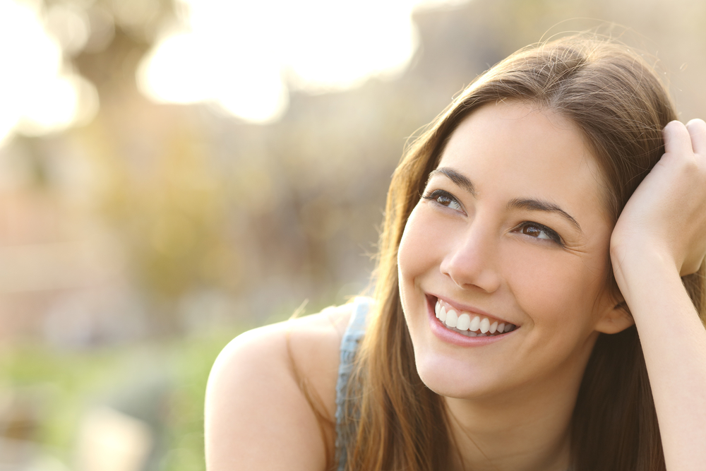 Woman smiling outdoors with her hand resting in her hair 
