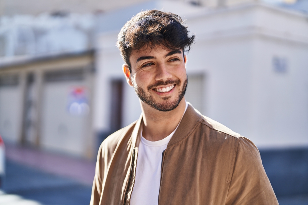 Natural-looking smile with customized cosmetic dental care Smiling young man outdoors, representing a natural-looking smile after cosmetic dental care in the San Marcos and San Diego community