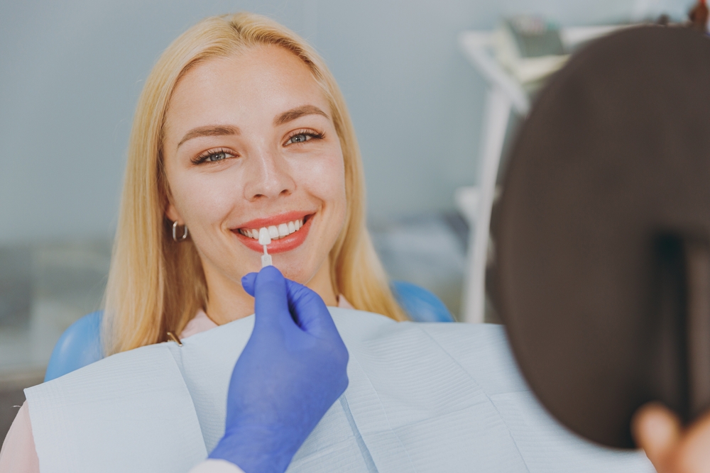 Custom veneer color matching Dentist holding a shade tab against a patient’s front teeth while planning custom dental veneers
