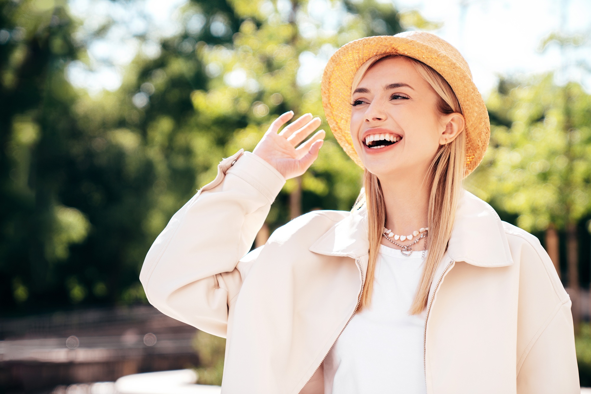 Woman laughing outdoors Woman in a straw hat laughing and waving outdoors among trees