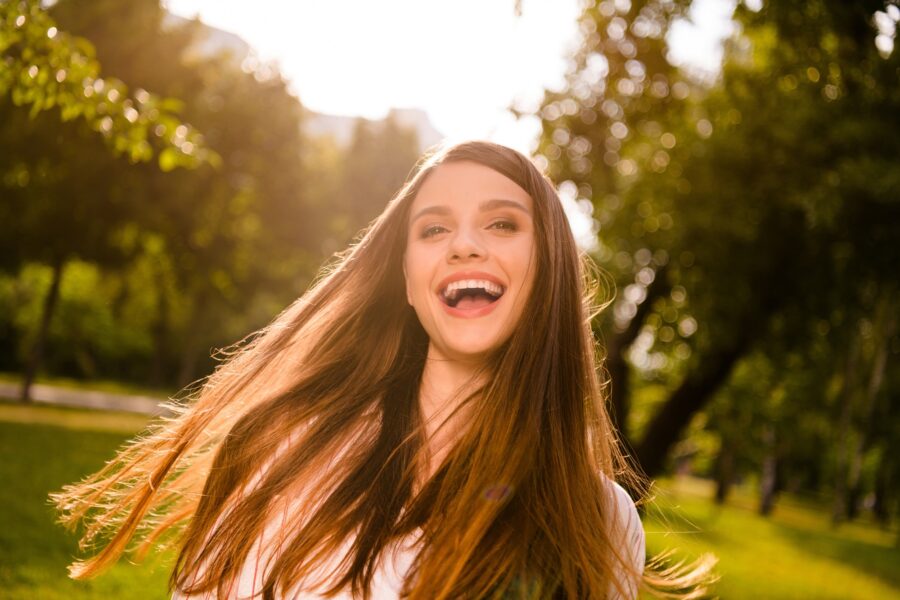 Woman with long hair laughing outdoors in a sunlit park