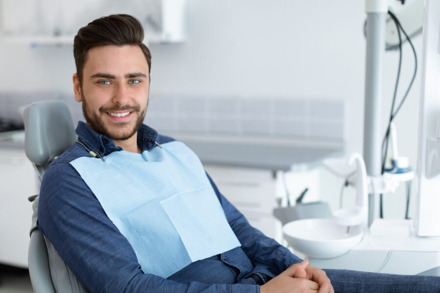 Smiling man in a dental bib seated in a treatment chair with hands folded in his lap