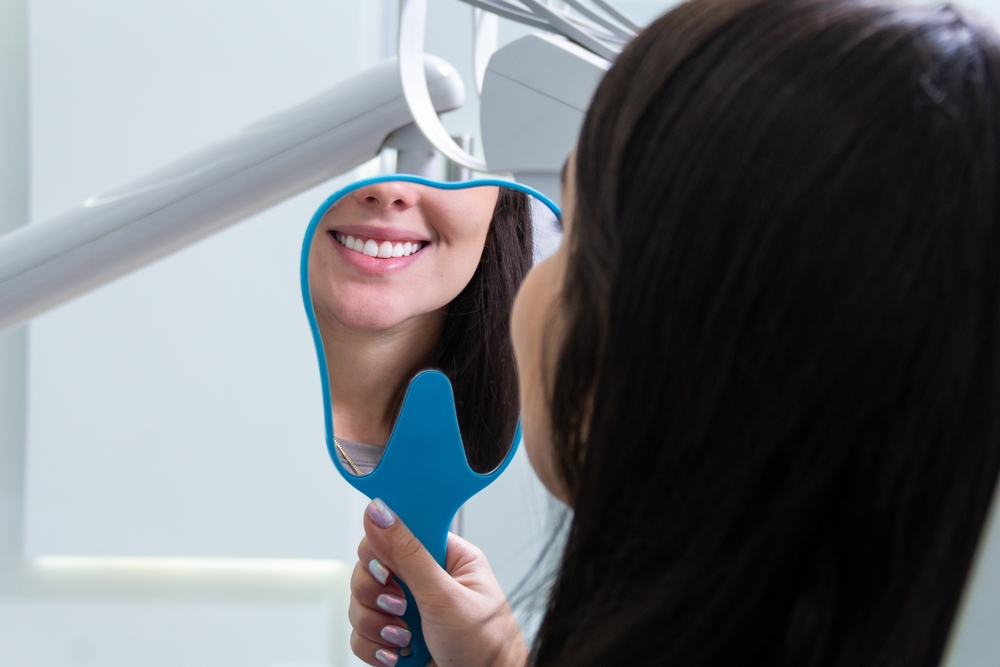 Patient holding a hand mirror to view her smiling reflection in a dental chair