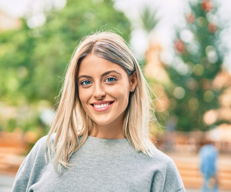 Blonde woman smiling outdoors in a gray sweater
