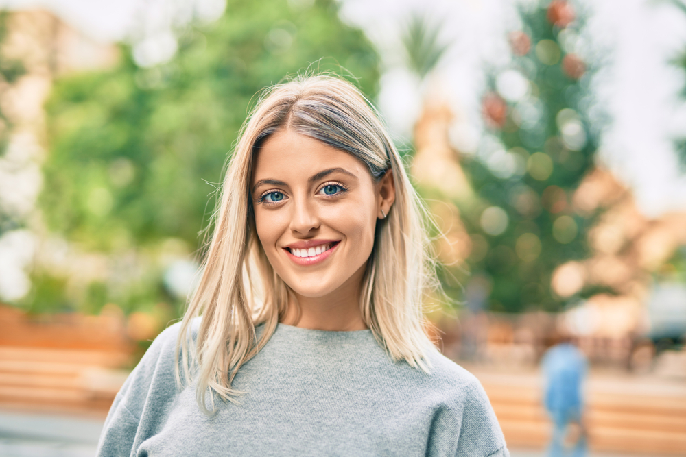 Blonde woman smiling outdoors in a gray sweater 
