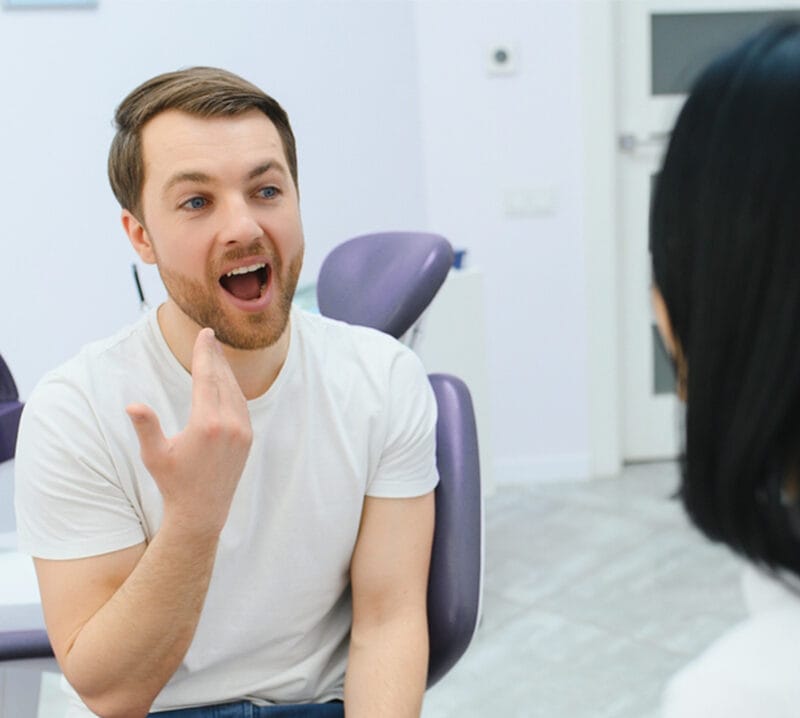 Dentist holding a tooth shade guide next to a reclined patient's smile
