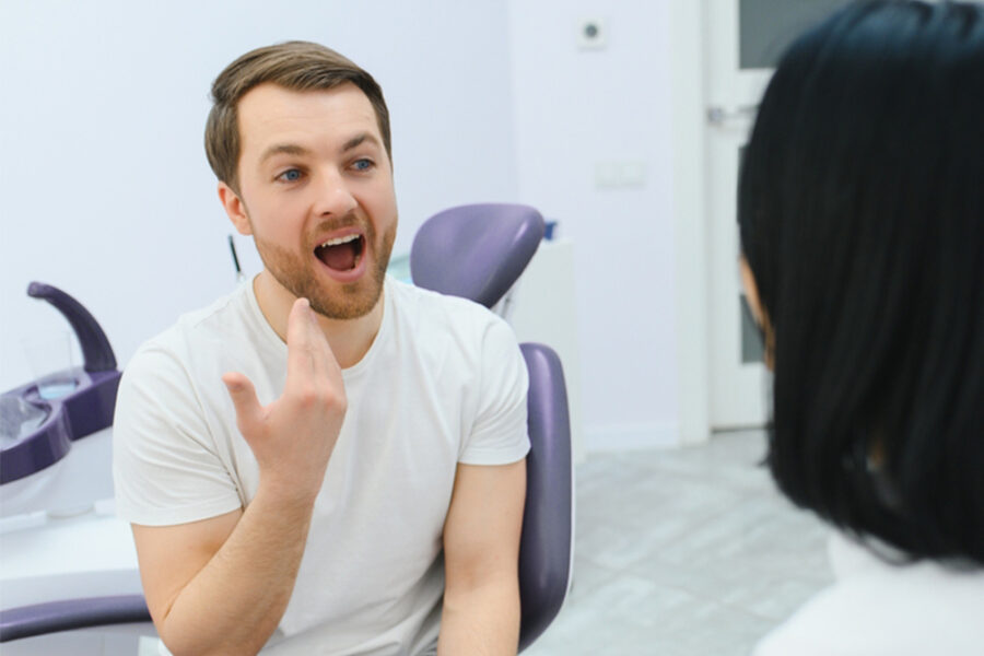 Dentist holding a tooth shade guide next to a reclined patient's smile