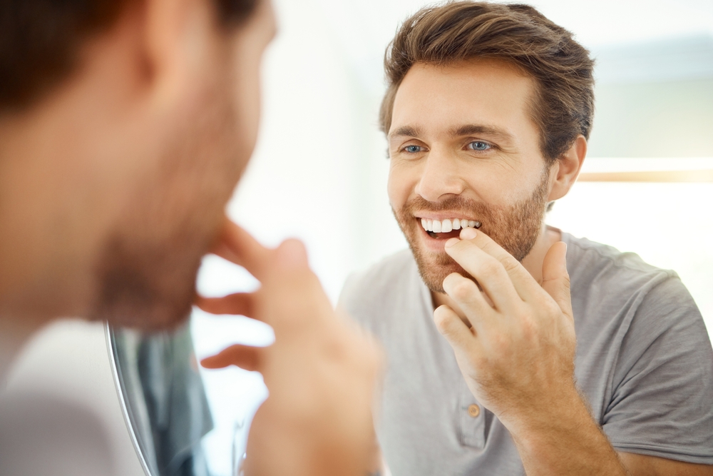 Man examining his smile in a mirror while considering cosmetic dental treatment in the San Marcos and San Diego community