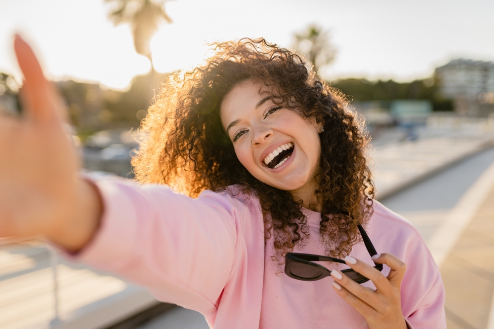 Smile confidence with personalized cosmetic dentistry Smiling woman taking a selfie outdoors, representing confidence after cosmetic dental care in the San Marcos and San Diego community