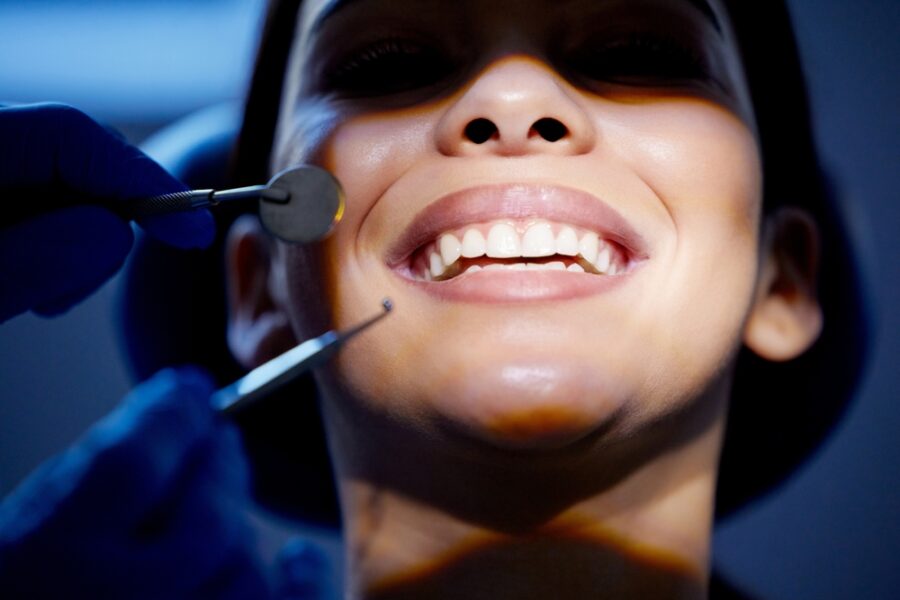 Gloved hands holding a dental mirror and scaler near a patient's smiling teeth