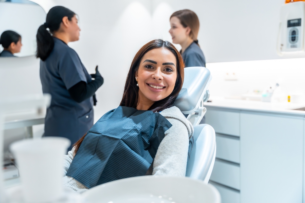 Smiling woman in a dental chair with staff conversing in the background