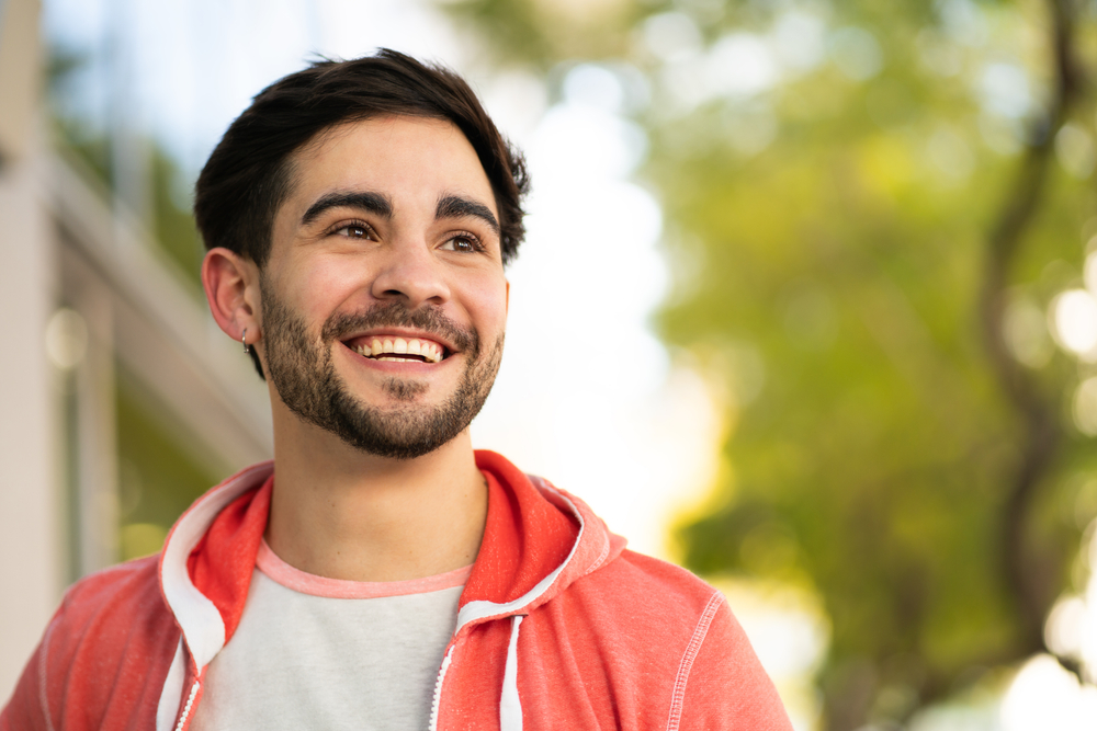 Man with a beard smiling outdoors in a red hoodie 
